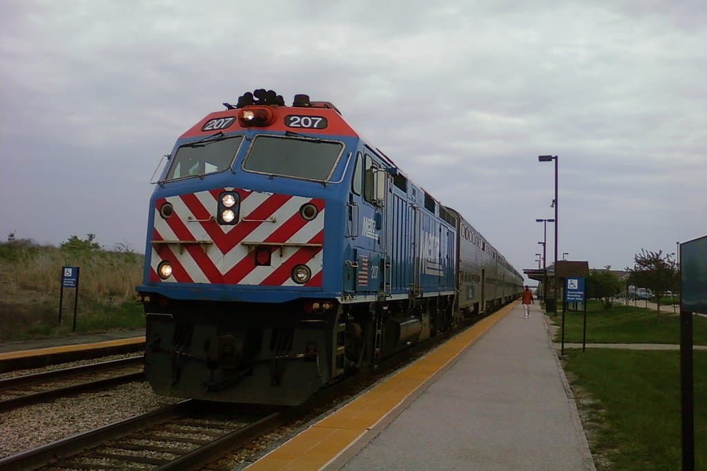 A Metra train pulling into the Hickory Creek station platform in Mokena under an overcast sky