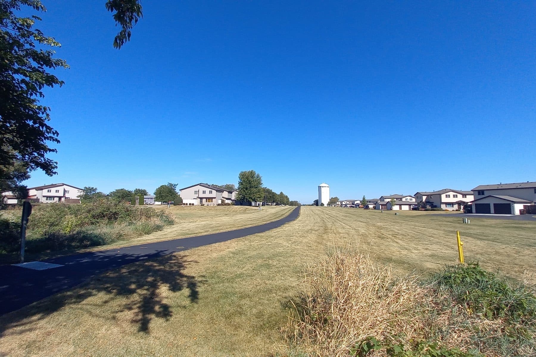 A paved bike trail running past two-story homes toward the New Lenox water tower under a clear sky